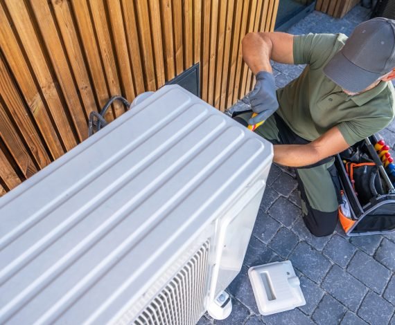 Technician Repairing Air Conditioning Unit Outside Modern Building on Sunny Day